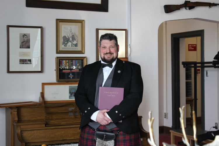 Aaron dressed in a formal bagpiping outfit holding a book of bagpipe tunes