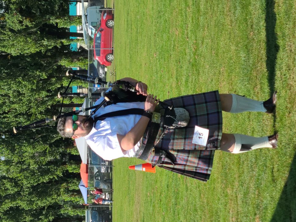 Aaron standing in a grassy field of a highland games competition playing the bagpipes